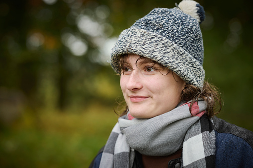 Young adult woman in a hat and yellow jacket breathing fresh air in the winter forest