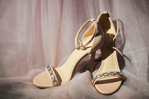 Beautiful women's sandals with beige rhinestones. The shoes stand against the fabric of the dress. Shoes for weddings or special events.