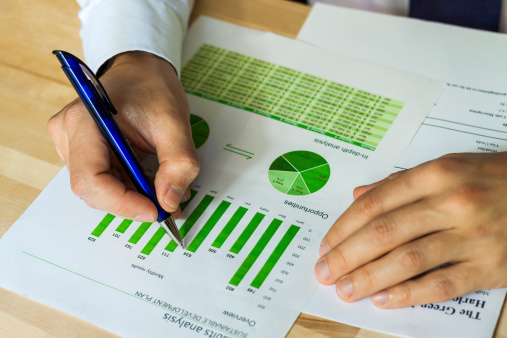 Businessman analyzing sustainable development opportunities charts at workspace. Hand holding a pen and green charts.