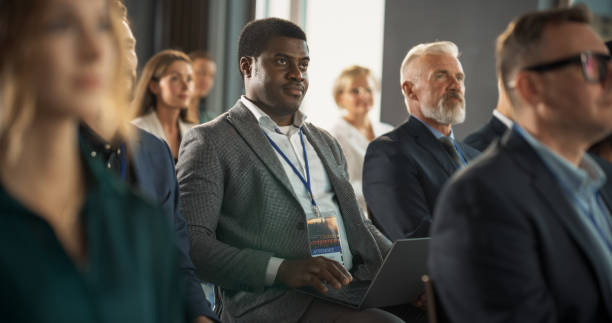 istock Black Man Sitting in a Crowded Audience at Business Conference. Corporate Delegate Using Laptop Computer While Listening to an Inspirational Entrepreneurship Presentation About Developing Markets. 1757727136