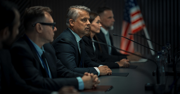 Caucasian Male Organization Representative Speaking at Economic Conference. Head Of The United States Delegation Delivering Speech at an International Political Summit. Diverse Delegates Listening.
