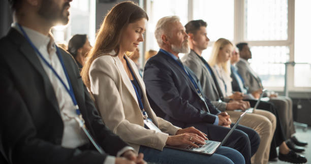 istock Female Journalist Sitting in Crowded Auditorium at a Tech Conference. Young Woman Using Laptop Computer. Reporter Watching Innovative Technology Presentation About New Software and High Tech Products. 1757741395