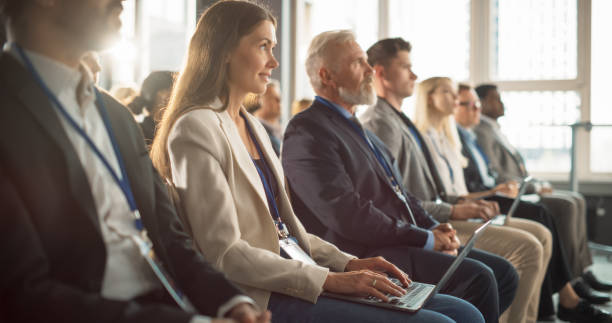 istock Female Journalist Sitting in Crowded Auditorium at a Tech Conference. Young Woman Using Laptop Computer. Reporter Watching Innovative Technology Presentation About New Software and High-Tech Products. 1757741938