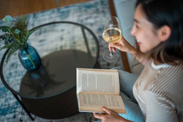 istock Woman  in Jeans Sitting  on a Sofa and Holding Open Book While Drinking Wine 1757746329