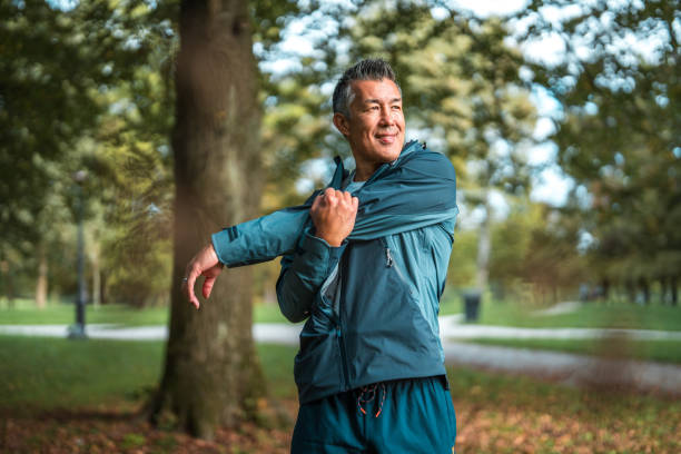 Asian Male Stretching at Park An Asian man in his mid-adult years practices outdoor fitness by stretching in a public park. adults exercising stock pictures, royalty-free photos & images