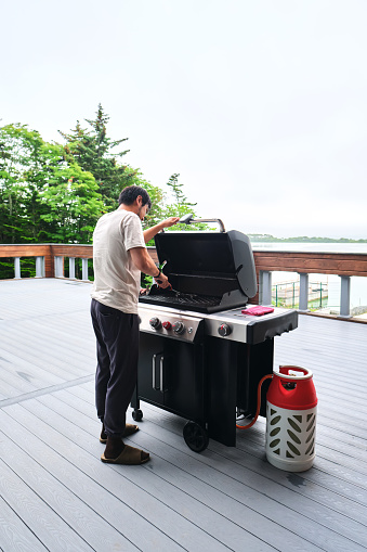 A man cooks on a grill on the veranda of his house.