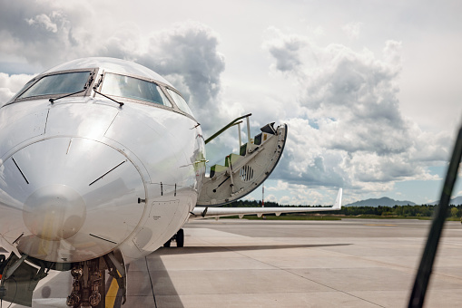 Close-up through the window front shot of a commercial airplane perfectly parked at the airport runway terminal with the passenger boarding stairs going down and getting ready to be used on a sunny day with blue sky and a little cloudy.