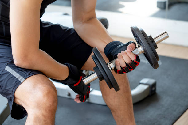 hombre deportivo con cuerpo bien entrenado en ropa deportiva negra con guantes deportivos sentado en el banco de entrenamiento levantando mancuernas en el gimnasio. concepto de entrenamiento con pesas y culturismo - weight training weight bench weightlifting men fotografías e imágenes de stock