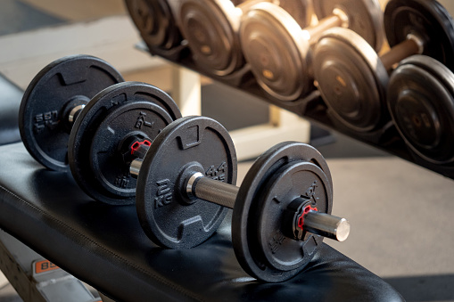 Dumbbells on black workout bench in fitness gym. Weight training equipment for physical exercise