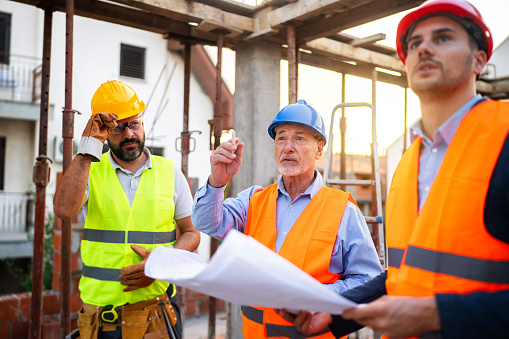 A group of male Caucasian architect, building contractor, and engineer, having a meeting on a construction site, where they looking at the blueprint