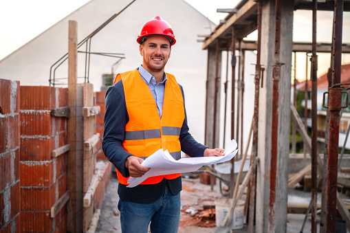 Architect wearing site safety gear and holding a set of plans whilst surveying a new building plot