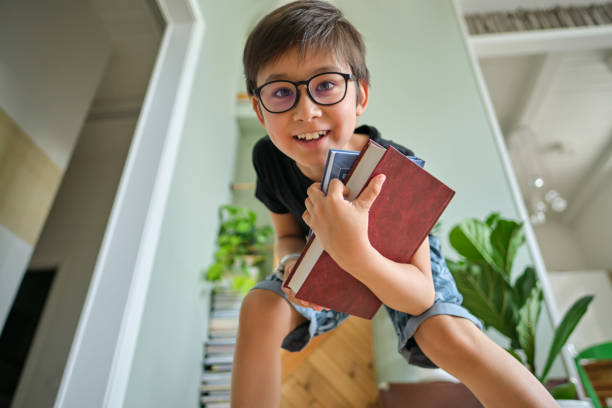 A boy holds a stack of books against the background home library.
