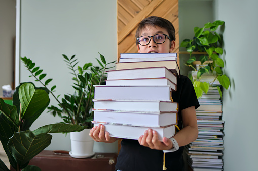 A boy holds a stack of books against the background of his home library.