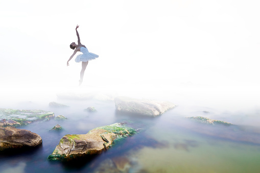 Ballerina dancing on the rocks in the fog