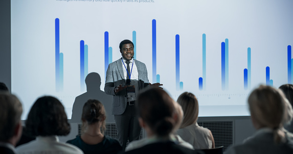Successful Black Businessman Giving Presentation At International Business Conference. African American Male Entrepreneur Pitching An Innovative Online Service Startup To Diverse Audience Of Investors