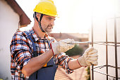 Caucasian construction worker using pliers to tighten the wire, while making rebar