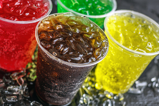 Una gran cantidad de refrescos en vasos de plástico coloridos y sabrosos con cubitos de hielo enfriados en hielo sobre el fondo negro, refrescos o bebidas carbonatadas en hielo photo