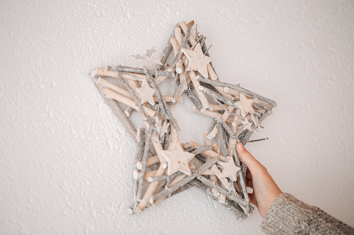 Christmas wreath.childrens hands hang a white wreath in the shape of a star on a white wall. girl in a white sweater holds a Christmas wreath in her hands.