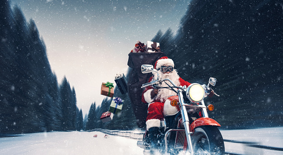 Unconventional biker Santa Claus riding a fast motorbike and delivering Christmas gifts