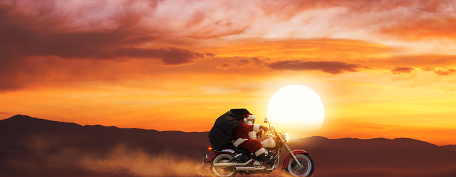 Adventurous Santa Claus riding a fast motorbike at sunset and carrying Christmas gifts