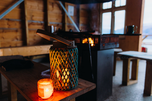 Scenic view of winter day in traditional wooden gapahuk in the mountains with warm candlelights and campfire in Scandinavia