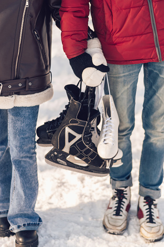 Young couple in love active date ice skating on the ice arena on a winter day.Teenagers go to an skating rink with skates in their hands,close up.Winter entertainment,leisure activity.