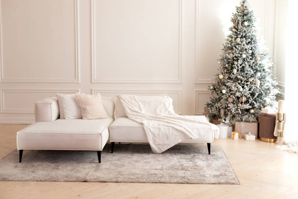 istock Comfortable couch with three cushions and a blanket standing in bright room interior with grey carpet in a modern interior. Modern interior living room with large light  corner sofa and Xmas tree. 1757910689