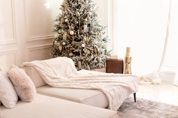 istock Modern interior living room with large light  corner sofa and Xmas tree. Comfortable couch with three cushions and a blanket standing in bright room interior with grey carpet in a modern interior. 1757910719