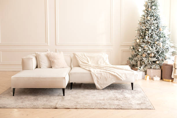 istock Modern interior living room with large light  corner sofa and Xmas tree. Comfortable couch with three cushions and a blanket standing in bright room interior with grey carpet in a modern interior. 1757911365