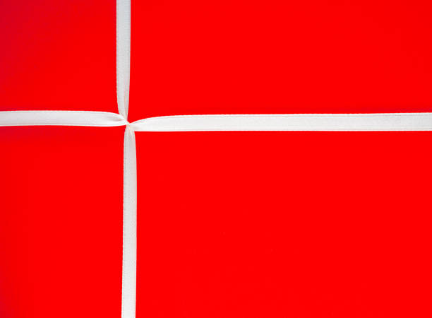 Macro image of a gift with white ribbon tied over bright red wrapping paper.