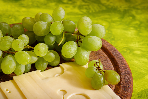 Tasty hard cheese with grape fruit on wooden cutting board