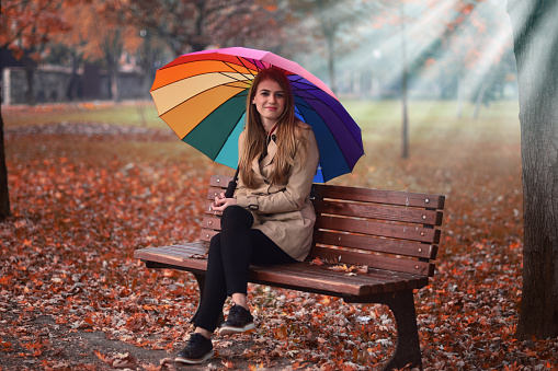 Young beautiful girl sitting on the bench in the autumn park with a umbrella.