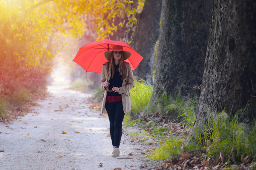 A young woman walks with a red umbrella on a sunny autumn day.