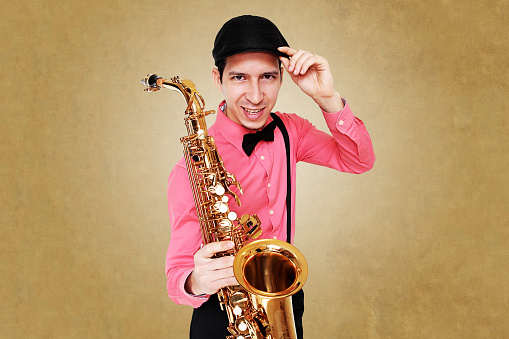 White male saxophonist wearing pink long sleeves shirt holding golden saxophone looking forward. Photo in studio.