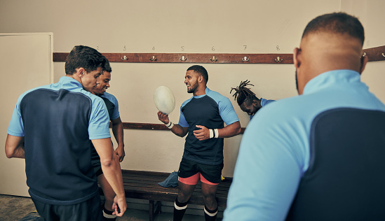 Locker room, motivation and team building, rugby players in strategy discussion or game plan with ball. Training, coaching and group of sports men planning teamwork with leader in cloakroom together.