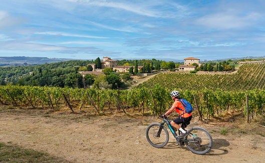 nice senior woman riding her electric mountain bike between olive and cypress trees in the Ghianti Area of Tuscany,Italy