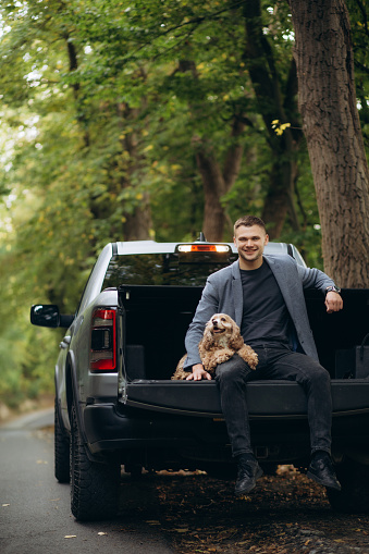 A man is sitting on a jeep pickup holding a dog in his arms