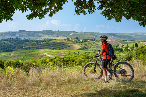active senior woman cycling with her electric mountain bike in the awesome landscapes of Tuscany, Italy