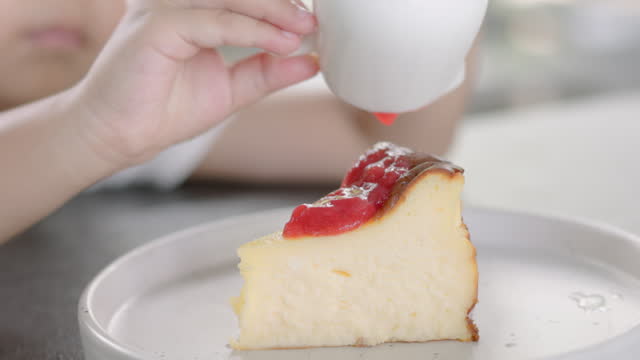Boy hands pouring strawberry sauce over cheese cake
