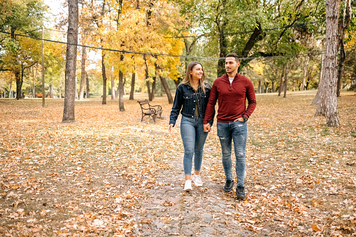 Young couple in love walking in city park on yellow leaves in Autumn