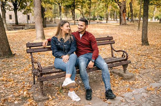 Young couple in love sitting in city park on yellow leaves in Autumn