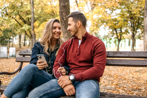 casal da geração millennial passando um tempo ao ar livre no outono ouvindo música juntos usando o telefone celular - heterosexual couple audio - fotografias e filmes do acervo