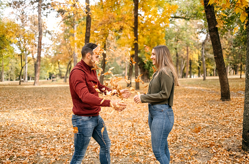 Young couple standing in city park on yellow leaves in Autumn