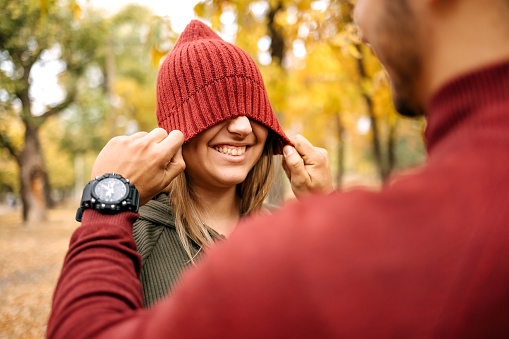 Young couple in love trying on cap in city park on yellow leaves in Autumn