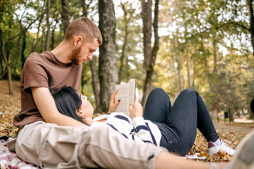 Young couple in love sitting on blanket in city park on yellow leaves in Autumn