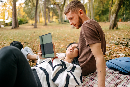 Young couple in love sitting on blanket in city park on yellow leaves in Autumn