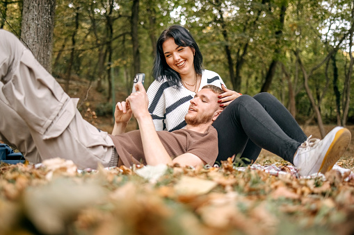 Young couple in love sitting in city park on yellow leaves in Autumn