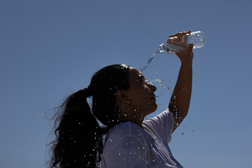 Woman pouring water overhead in hot summer day to refresh herself after running