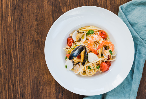 Pasta spaghetti with shrimps, mussels, clams on wooden table. Italian typical spaghetti recipe with seafood and tomatoes.