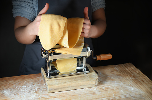 Pasta maker machine, woman's hands prepare fresh pasta sheets for tagliatelle, ravioli or lasagna.